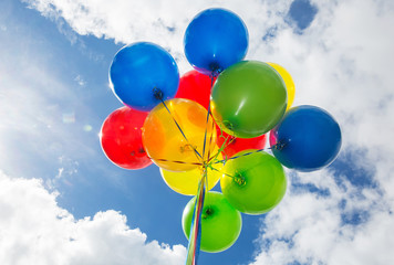 Cluster of colorful balloons under a sunny blue sky with puffy w