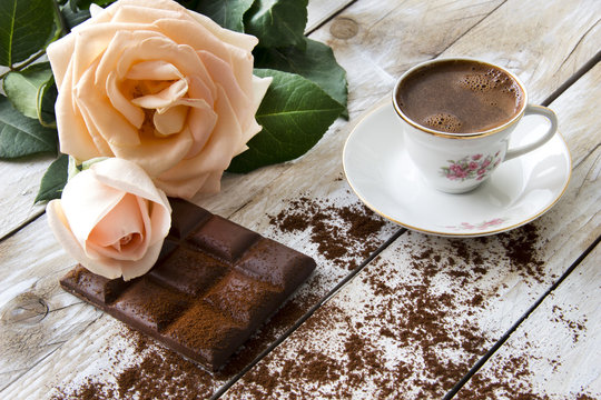 Turkish coffee with peach-colored rose and slices of chocolate on the wooden table 