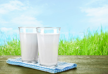 Glasses of milk on wooden table against grass and blue sky background