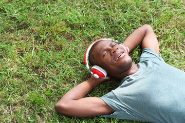 Handsome African American man with headphones lying on green grass