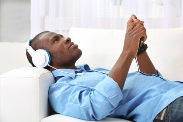Handsome African American man with headphones lying on sofa in room