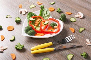 Useful cut vegetables on a plate in the form of heart on wooden table top view