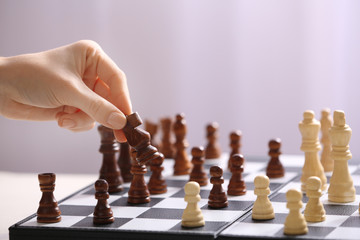 Female hand playing chess on light blurred background