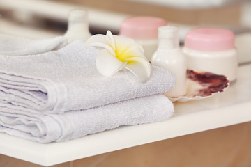 Obraz na płótnie Canvas White towels with cream and tropical flower on a shelf in bathroom