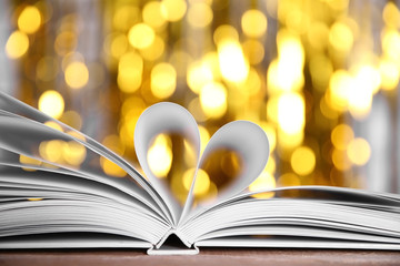 Sheets of book curved into heart shape on wooden table against unfocused lights