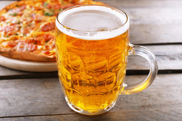 Tasty pizza and glass of beer are on wooden table, close up