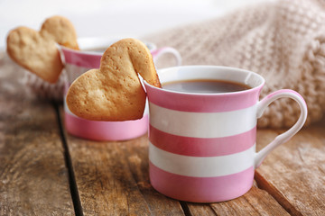 Heart shape cookie on cup of coffee on wooden table closeup