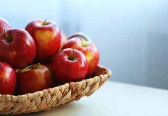 Ripe red apples in wicker basket on a kitchen table