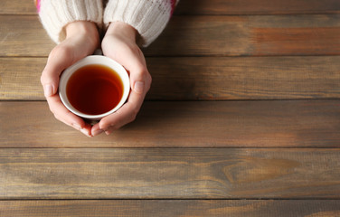 Female hands holding cup of tea on wooden background