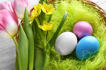 Easter eggs in nest with spring flowers on white wooden table