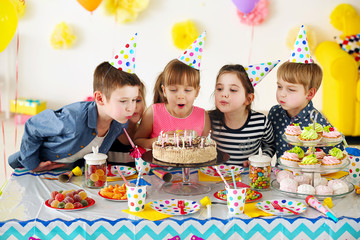 Happy group of children blowing candles on cake at birthday party