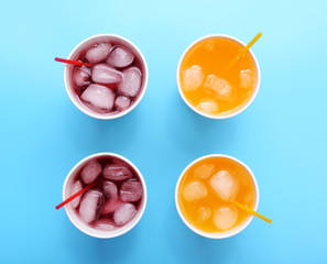 Orange and pomegranate drink with ice cubes on blue background, top view