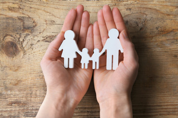 Cutout figurine of a family in female hands on wooden background