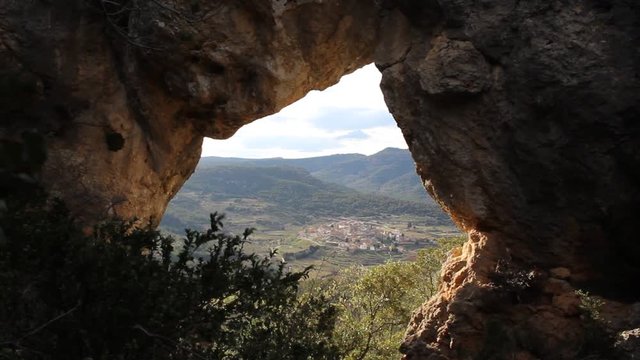 View through mountain hole to village in Catalonia, north Spain. Rocks and green plants surrounding natural hole in mountain.