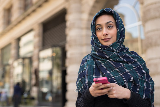 Young woman wearing hijab in city texting on cell phone