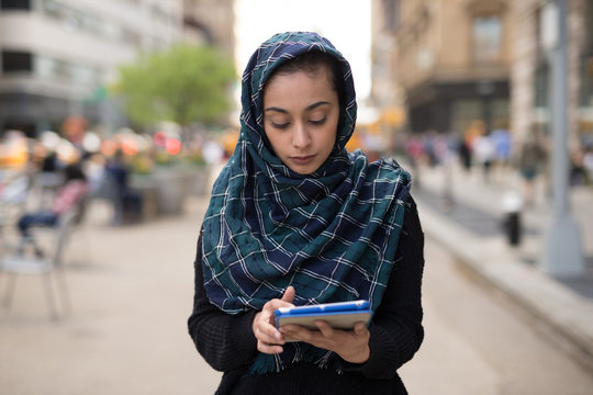 Young woman wearing hijab in city using tablet computer