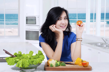 Beautiful girl holds tomato in kitchen