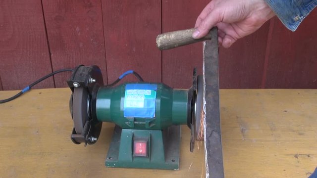 

Man sharpening old handmade debarker with stone grinder