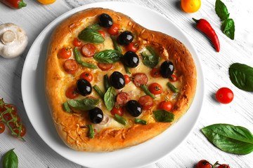 Fresh tasty heart shaped pizza decorated with vegetables and herbs on wooden background