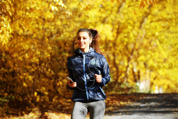 Young beautiful woman running in autumn park and listening to music with headphones.