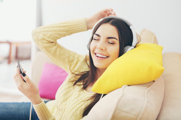 Happy young woman with headphones listening to music on a sofa at home