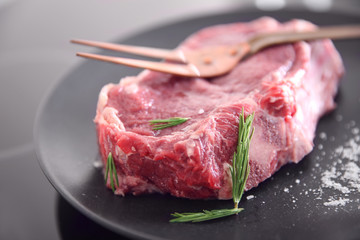 Raw pork steak with meat fork and rosemary on black plate