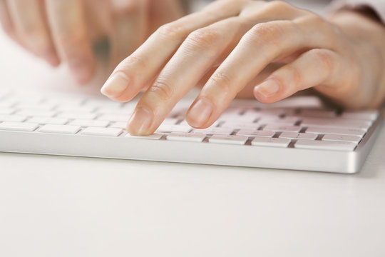 Female hands using keyboard on white wooden table, close up