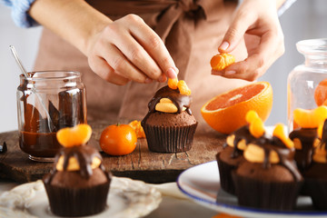 Obraz na płótnie Canvas Female baker decorating tasty cupcake with slice of mandarin and chocolate on the table