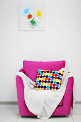 Pink armchair with blanket and pillow on light wall background