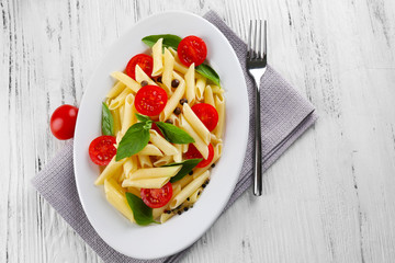 Plate of pasta with cherry tomatoes and basil leaves on wooden table, top view
