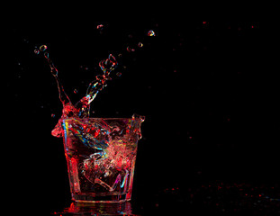 cocktail in glass with splashes on dark background. Party club entertainment. Mixed light.