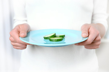 Female hands holding a plate with slices of cucumber.