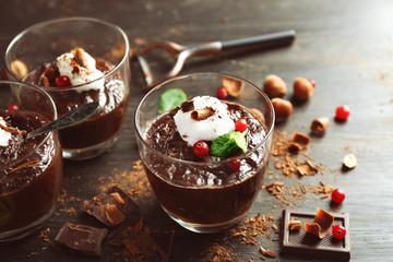 Glass cups of chocolate dessert with cranberries, fresh mint and frothed milk on black wooden table