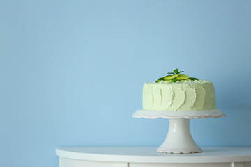 Big lime cake on a white stand beside light blue wall