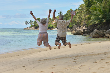 elderly couple jumping at tropical beach