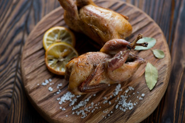 Close-up of whole baked quails on a rustic wooden chopping board