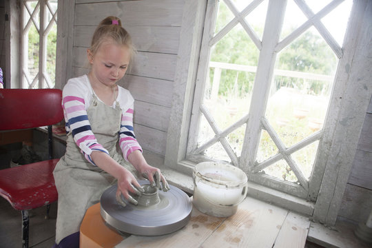 Girl playing with clay at potters wheel