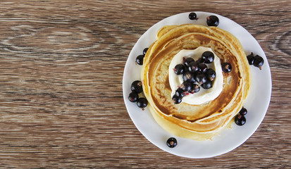 Pancakes with the cream and blackcurrant on the wooden table