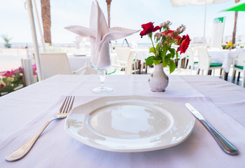 Plate, fork, knife, napkin and flowers on the cafe  table.