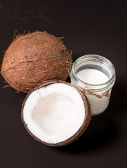 Coconut with coconut oil in jar on black background