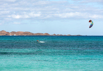  Unknown kitesurfer surfing on a flat azure water of Atlantic ocean in Corralejo, Fuerteventura, Canary islands, Spain