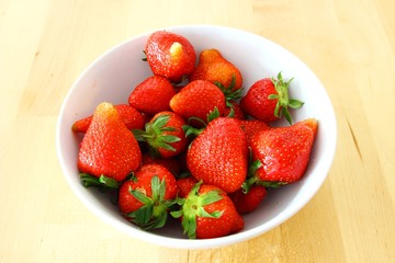 Strawberries in white bowl on wooden table