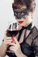 Schöne Frau mit Maske hält ein Glas Rotwein