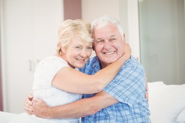 Senior couple looking away while embracing in bedroom