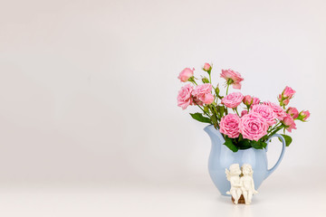 Pink flowers in blue jug. Roses in jug. Two angels on wooden banch.