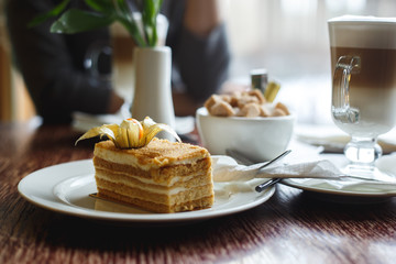 Piece of cake, sugar-bowl and cup of latte coffee in a cafe on the blur background of city