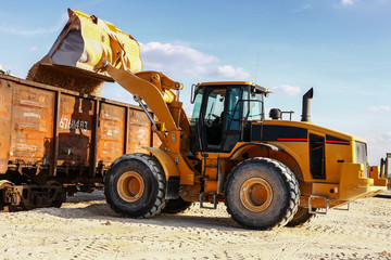 Loader loads the wagon train transport against cloud sky