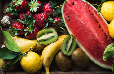 Various colorful tropical fruit selection in wooden tray over dark background