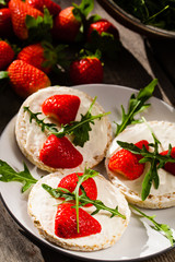Multigrain rice cakes with strawberries fruit , soft mascarpone cheese and arugula for healthy breakfast.