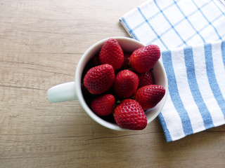 Red fresh strawberries in white pottery cup on wooden table